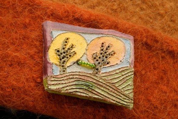 KaufmannRaku Jane Kaufmann raku landscape button adorns an orange knit felt hat by Carrie Cahill Mulligan, of Canaan, New Hampshire.